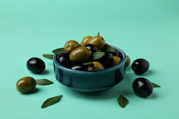 Bowl of olives and leaves on mint background