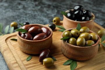Board with olives and leaves on black smokey background