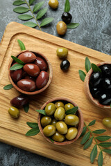 Board with olives and leaves on black smokey background