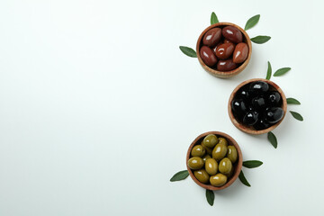 Wooden bowls of olives and leaves on white background