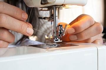 young woman putting thread on needle of sewing machine