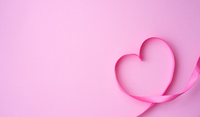 Pink ribbon folded in the shape of a heart on a pink background. Love and valentine's day concept