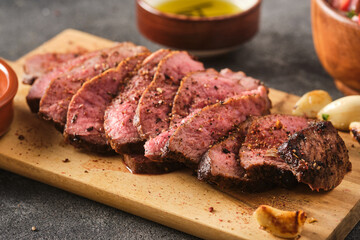 Sliced BBQ steak medium rare with salad and garlic on the grey background. Hip steak on wooden board