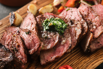 Sliced BBQ steak medium rare with salad and garlic on the grey background. Hip steak on wooden board
