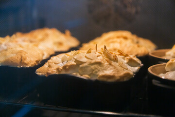 Fish in casseroles with meringue almond topping being cooked in the oven.