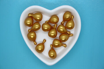 Capsule gold oil for face in the white plate in the shape of a heart.