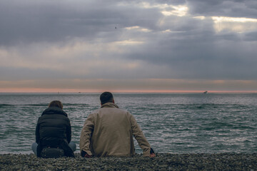 young couple sitting on the beach on the background of the sea back view