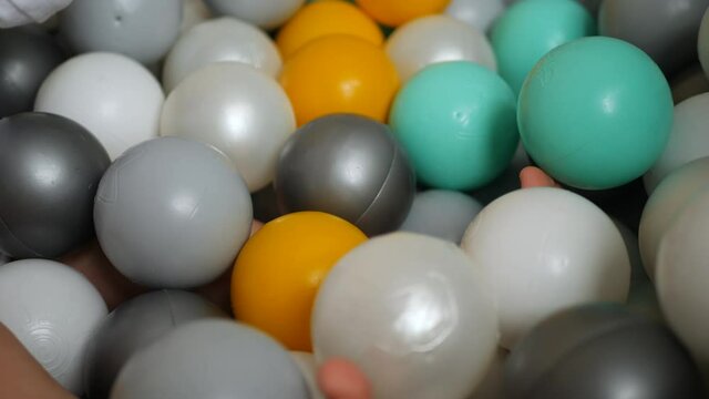 girl in a white bodysuit plays with colorful plastic balls in dry pool