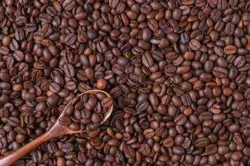 A dark wooden spoon lies on coffee beans, coffee beans are inside the spoon