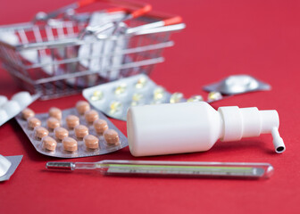 Spray, vitamins, Blister pack of pills , bottle lying near blurred mini basket on red background. Pharmacy Shopping Concept, copy space, banner. medicine background. High quality photo. 