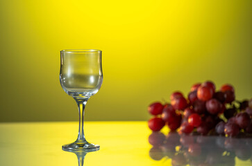 Empty Wineglass and the grapes are on the reflection table. Yellow background. Summer mood. Nice day