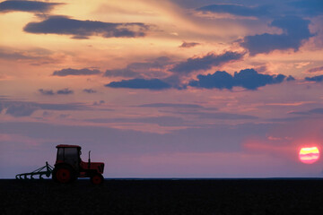Colorful sunset landscape with tractor working on a field