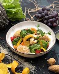 Exotic mixed salad of meat croquettes, lettuce, bell peppers, tomatoes and oranges garnished with microgreen peas. Vitamin assorted in bowl on black table.