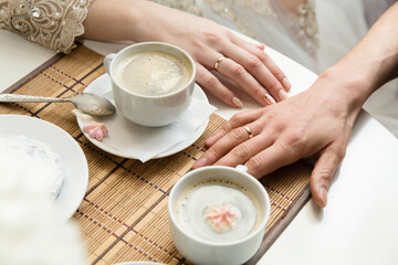 white cups of coffee on the table and hands in wedding rings