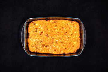 Cottage cheese casserole with raisins, carrots and dried apricots in a glass pan on a black tablecloth top view