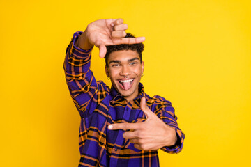 Photo of young cheerful afro man happy smile grimace tongue-out make fingers frame snapshot isolated over yellow color background