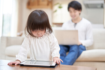 自宅で仕事をするパパと、1人でタブレットを見るアジア人の子供