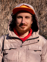 Bearded hipster guy millennial in orange snapback on nature background on spring sunny day. Funny red beard male face