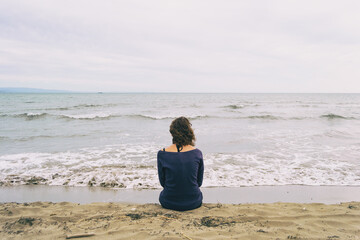 girl sitting on the sand on the shore of the beach looking at the horizon of the sea