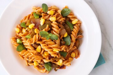 Whole wheat fusilli Pasta Arrabbiata with vegetables. Vegetable Pasta with zucchini, mushrooms, corn, and peppers on a white plate. on a white marble table with cutlery. copy space.