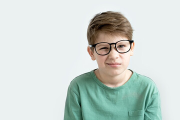 Surprised boy in a green T-shirt and glasses pensive scratches his head. Copy space.