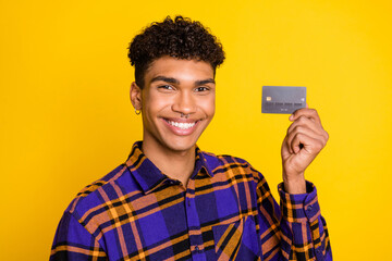 Photo of young african man happy positive smile hold credit card buy customer isolated over yellow...