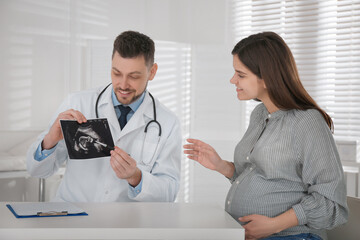 Gynecologist showing ultrasound picture to pregnant woman in clinic