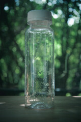 Selective focus image of empty plastic bottle with white lid, water drops in glass