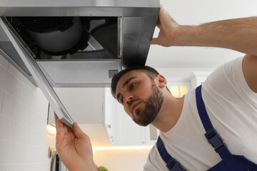Worker repairing modern cooker hood in kitchen