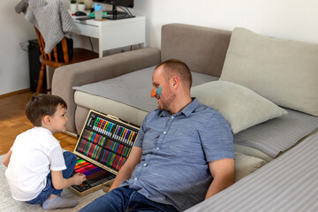 Obraz premium Cute little boy making colorful face on his father. Photo of a young father and his son enjoy the painting at home. Shot of a father and son doing arts and crafts at home. Dad and son having fun.
