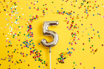 five years birthday party. number five with multicolored confetti in the form of stars on a yellow...