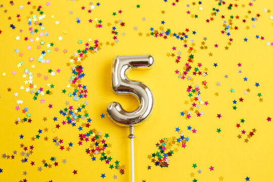 five years birthday party. number five with multicolored confetti in the form of stars on a yellow background