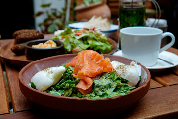 Close up shot of poached eggs and smoked salmon with spinach and falafel with salad on background. Breakfast options of fusion cuisine restaurant. Copy space, top view, background.