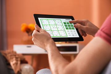 Man playing sudoku game on tablet indoors, closeup