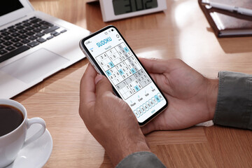 Man playing sudoku game on smartphone indoors, closeup