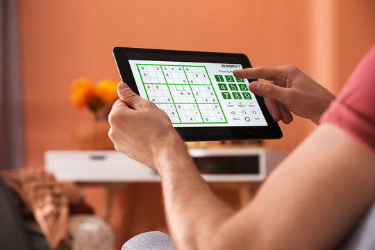 Man playing sudoku game on tablet indoors, closeup