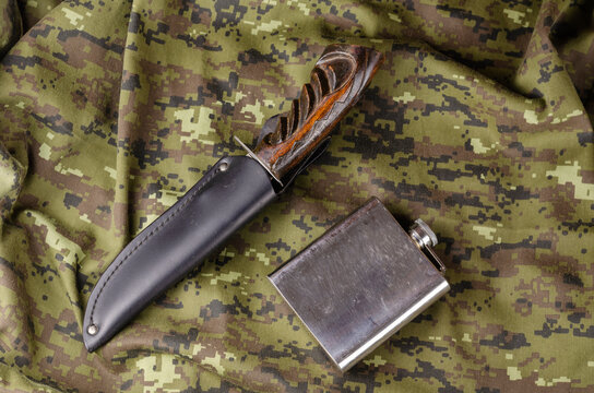 A knife with a wooden handle in a leather sheath and a metal fla