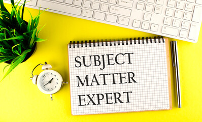 Subject Matter Expert text on notebook with keyboard , pen and alarm clock on the yellow background
