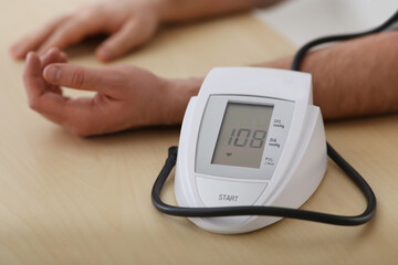 man checking blood pressure at wooden table indoors, closeup