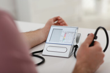Man checking blood pressure at table indoors, closeup