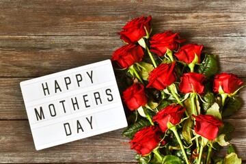light box with the text HAPPY MOTHER'S DAY and red roses on a wooden background. The concept of the holiday.