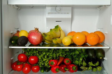 Fridge full of different fresh organic fruits and vegetables. Refrigerator shelves stacked with raw plant based dieting products. Close up, copy space, background.