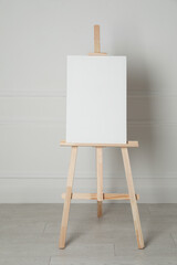 Wooden easel with blank canvas near light wall