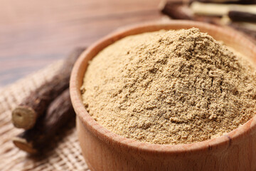 Powder in bowl and dried sticks of liquorice root on table, closeup