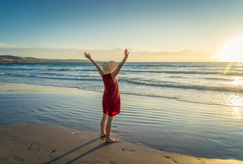 Fototapeta na wymiar Woman in red with arms outstretched by the sea at sunrise enjoying freedom and life