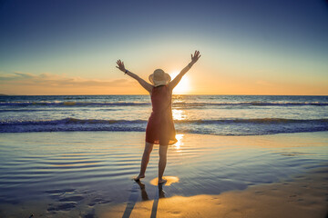 Woman in red with arms outstretched by the sea at sunrise enjoying freedom and life
