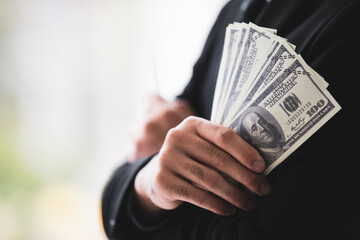 Closeup shot of United States of America hundred dollars banknotes currency in successful rich wealth male businessman cross arms wears black formal suit hand with blurred background