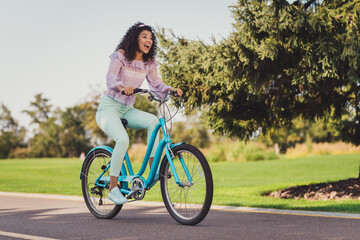 Full size photo of impressed brunette lady ride bicycle wear lilac top pants sneakers outside in park