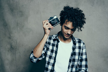 Fototapeta premium young man with a camera in hand and in a plaid t-shirt on a gray background indoors photographer