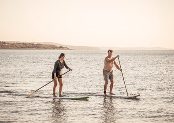 Mature couple on SUP, stand up paddle board, having fun on quiet sea at sunset